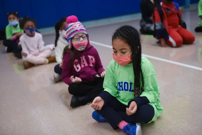 Children sitting on the floor, meditating, while wearing masks